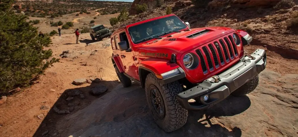 Red Jeep Wrangler driving up a steep dirt hill.