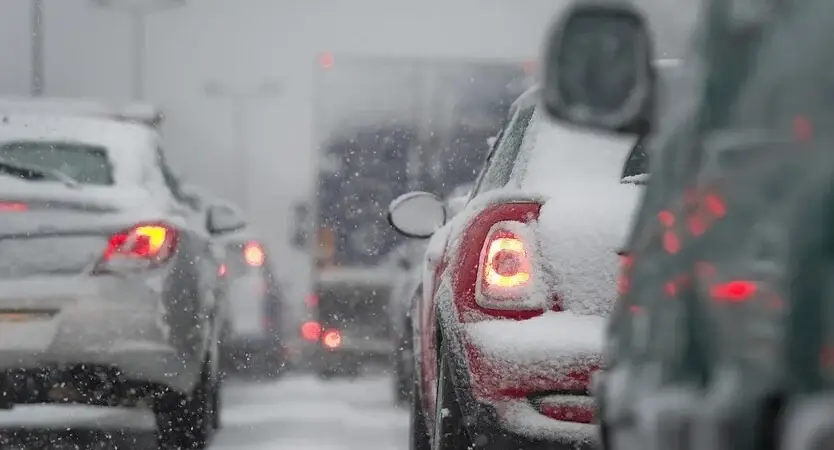 Close up of car rear break light with various other cars in front while driving in the snow
