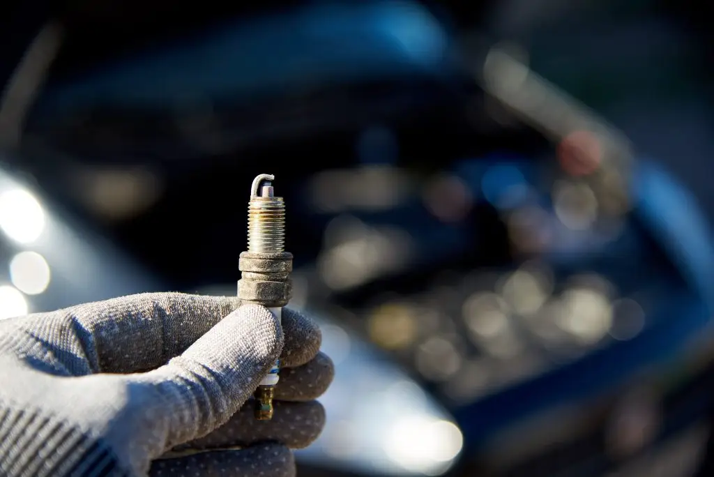 Spark plug for engine in male hand on the background of a car with an open hood.